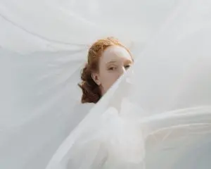 Bridal portrait of a red-haired bride in soft white tulle with glowing, luminous skin